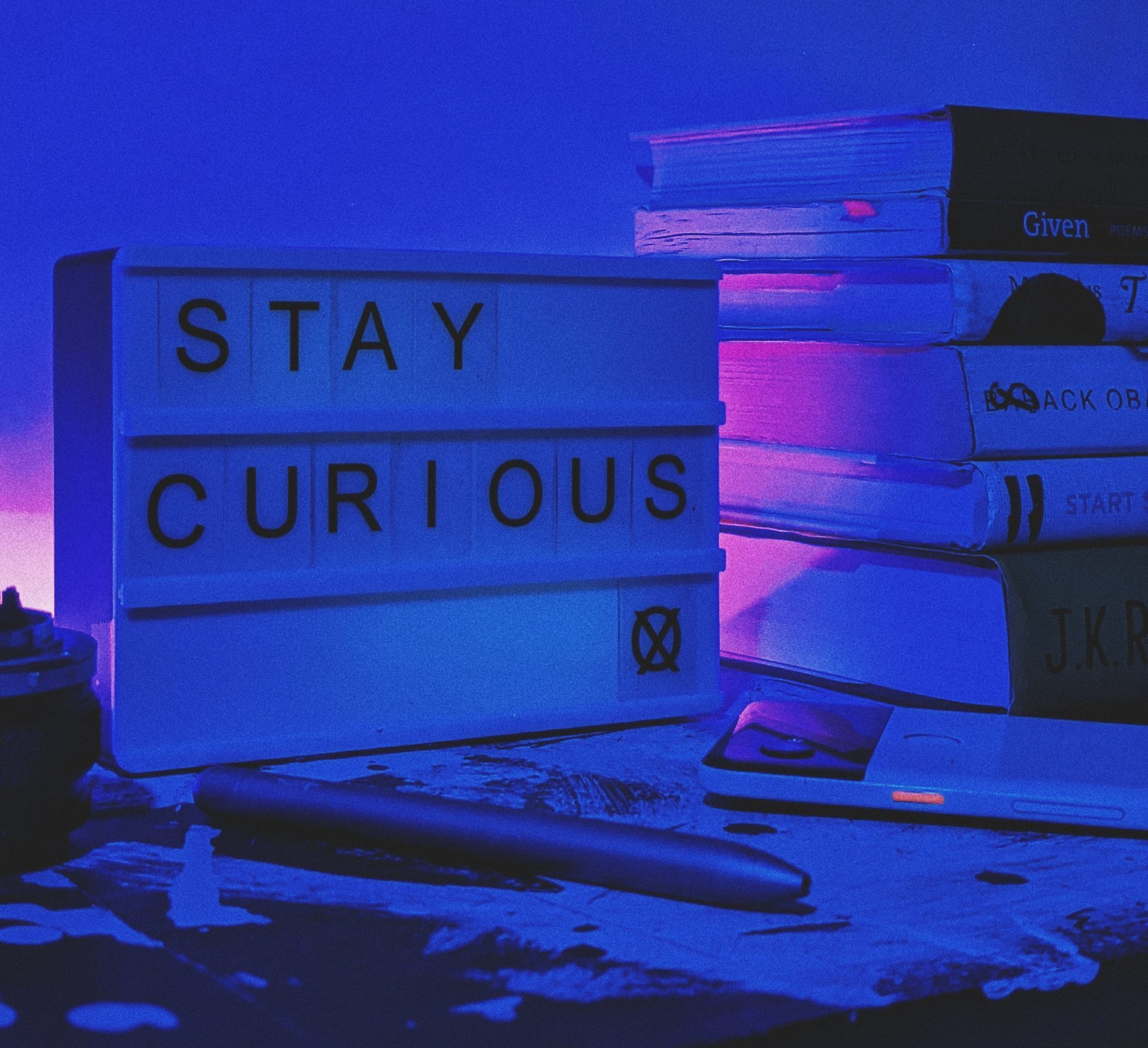 justin-heap-FY452QNxaNA-unsplash A sign reading "stay curious" in front of a stack of books